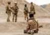 Second Crisis Risk — Stockpiles Running On Fumes Military personnel in tactical gear discussing in a desert-like environment