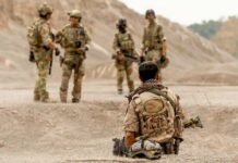 Military personnel in tactical gear discussing in a desert-like environment
