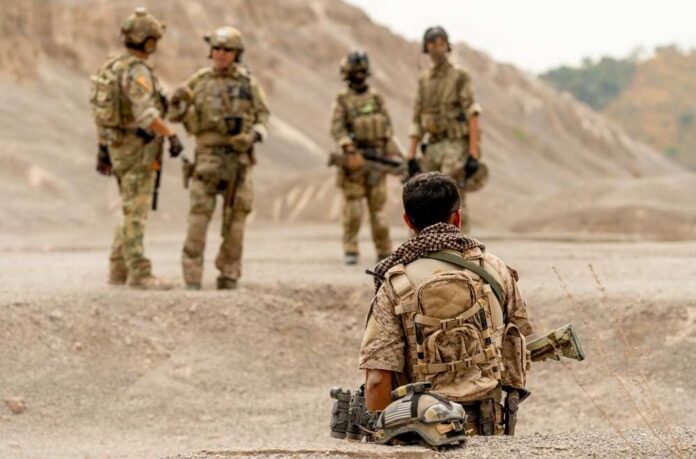 Back,Of,Man,As,Military,Or,Soldier,Look,To,Group Military personnel in tactical gear discussing in a desert-like environment