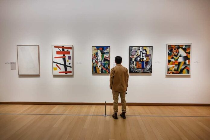 A person standing in an art gallery, observing various modern art pieces on the wall