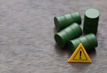 Antitrust Dogs Circle Big Oil Four green barrels and a warning sign on a wooden surface