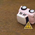 Car Payments Explode — House Money Now? Upside down pink toy car next to a warning sign