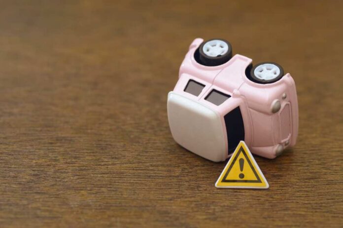 Overturned,Vehicle,Beside,Emergency,Warning,Sign,Representing,Crash,,Breakdown,,And Upside down pink toy car next to a warning sign