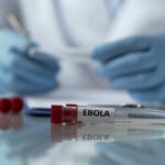 2,000 Dead — More Coming? Ebola test tubes on lab table with gloved scientist in background