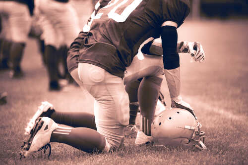 Vintage,Toned,Image,Of,American,Football,Players,In,Action Football player kneeling on the field with a helmet beside them