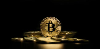 Gold Bitcoin coin on pile, dark background.