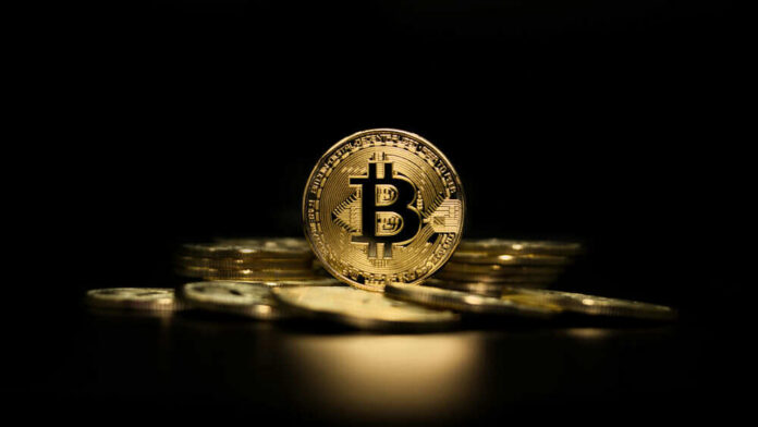 shutterstock_1902390253 Gold Bitcoin coin on pile, dark background.
