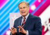 Extradition Standoff: Governor Abbott Holds The Clock Greg Abbott in suit speaking at an event.