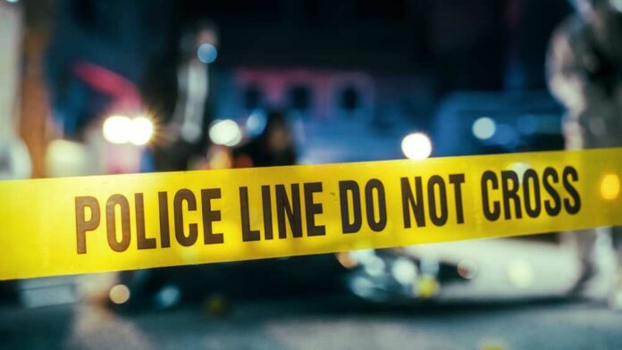 Police line caution tape at a crime scene with blurred figures in the background