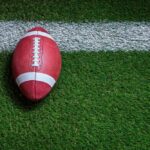 Football player kneeling on the field with a helmet beside them