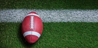 Football player kneeling on the field with a helmet beside them