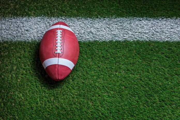Football player kneeling on the field with a helmet beside them