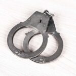 A pair of metallic handcuffs resting on a light wooden surface