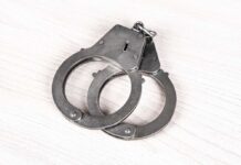 A pair of metallic handcuffs resting on a light wooden surface