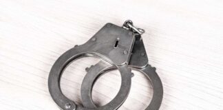 A pair of metallic handcuffs resting on a light wooden surface