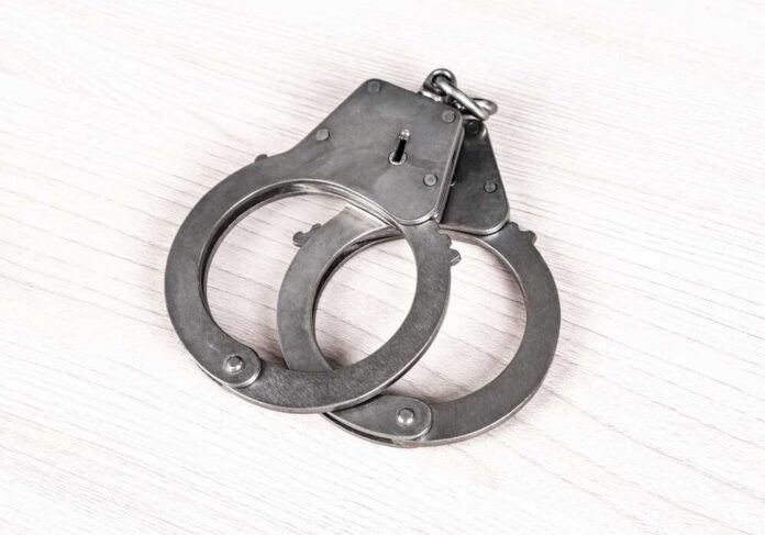 Closed,Handcuffs,On,The,Wooden,Table,Closeup A pair of metallic handcuffs resting on a light wooden surface
