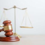 A wooden gavel in front of a balance scale symbolizing justice