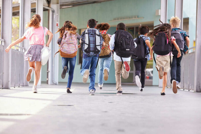Children running with backpacks outside a school building.