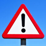 Federal Safety Net Feels Rigged A triangular warning sign with an exclamation mark against a blue sky