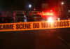 Crime scene tape with emergency vehicles in background.