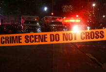 Predawn Gunfire Hits College Dorms Crime scene tape with emergency vehicles in background.