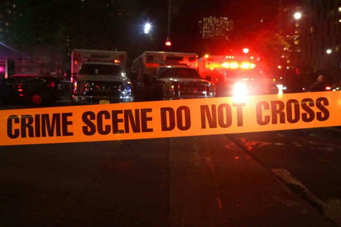 shutterstock_746018290 Crime scene tape with emergency vehicles in background.