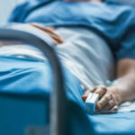 A patient lying in a hospital bed with a monitoring device in hand