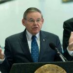 Robert Menendez speaking at a podium with hands raised