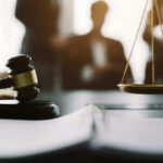 Gavel and scales in courtroom with blurred figures behind.
