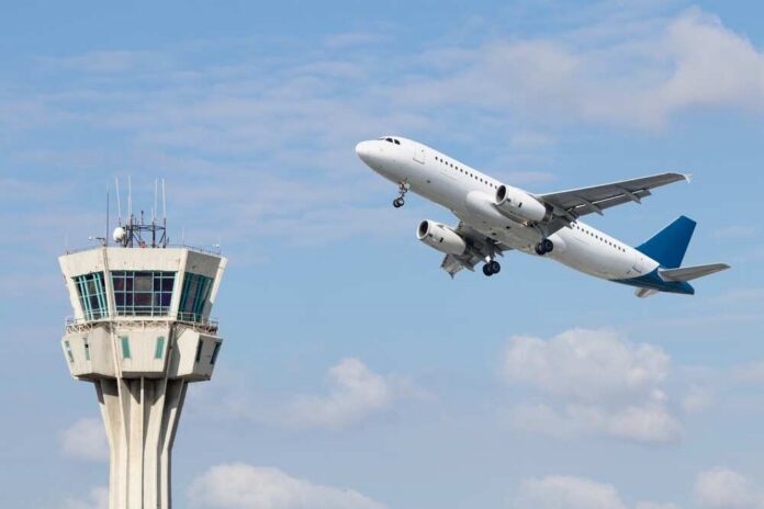 Air,Control,Tower,And,Airplane,On,Blue,And,Cloudy,Sky An airplane taking off near an airport control tower