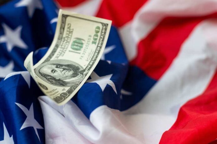 American,Striped,Flag,And,A,Stack,Of,One,Hundred,Dollar A hundred dollar bill resting on an American flag