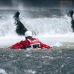 Rescuer in red gear navigating turbulent water near a waterfall