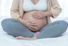 Pregnant Workers Punished By THIS Company? Pregnant woman sitting crosslegged on bed