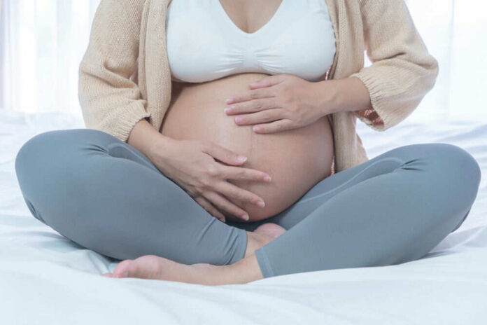 Pregnant woman sitting crosslegged on bed