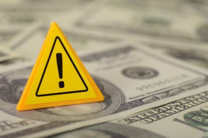 A yellow warning sign placed on a pile of dollar bills