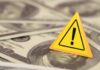 WARNING: $120 Ahead; Americans Slammed A yellow warning sign on a background of dollar bills