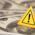 WARNING: $120 Ahead; Americans Slammed A yellow warning sign on a background of dollar bills
