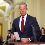 John Thune holds a note card while Tom Cotton speaks in the background