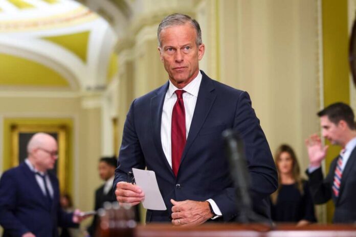 John Thune holds a note card while Tom Cotton speaks in the background