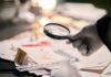 Gloved hand holding a magnifying glass over scattered forensic documents