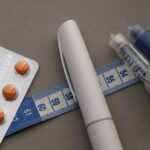 Medication blister pack, insulin pens, and tape measure on a gray surface