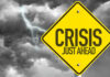Bus Chaos Looms — Pay Skyrockets Yellow sign reading Crisis Just Ahead with stormy sky