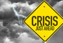 Yellow sign reading Crisis Just Ahead with stormy sky