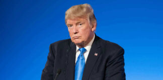 Man in suit with blue background speaking at podium.