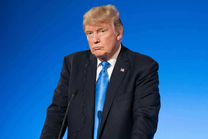 shutterstock_677261236 Man in suit with blue background speaking at podium.