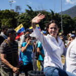 María Corina Machado waving in a street march alongside Teddy Williams