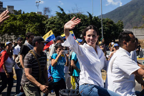 María Corina Machado waving in a street march alongside Teddy Williams
