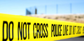 Police do not cross tape stretched across an outdoor scene