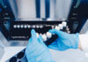 Person in blue gloves handling test tubes in a laboratory
