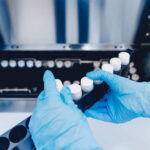 Person in blue gloves handling test tubes in a laboratory